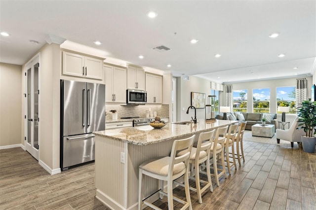 kitchen with a breakfast bar, sink, light hardwood / wood-style flooring, an island with sink, and appliances with stainless steel finishes