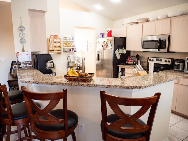 kitchen with a breakfast bar, light stone countertops, light tile patterned floors, appliances with stainless steel finishes, and kitchen peninsula