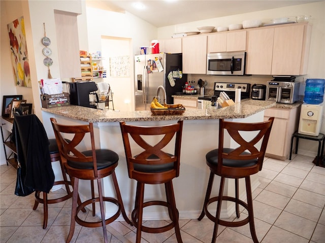 kitchen featuring a breakfast bar, light tile patterned floors, appliances with stainless steel finishes, light stone counters, and kitchen peninsula