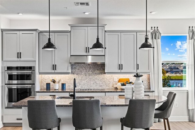 kitchen featuring gray cabinets, light stone countertops, and hanging light fixtures