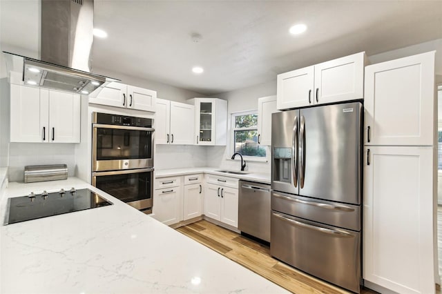 kitchen with light stone countertops, appliances with stainless steel finishes, island range hood, white cabinets, and light hardwood / wood-style floors