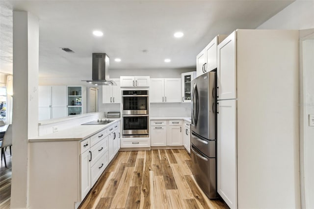 kitchen featuring island exhaust hood, appliances with stainless steel finishes, light wood-type flooring, kitchen peninsula, and white cabinets