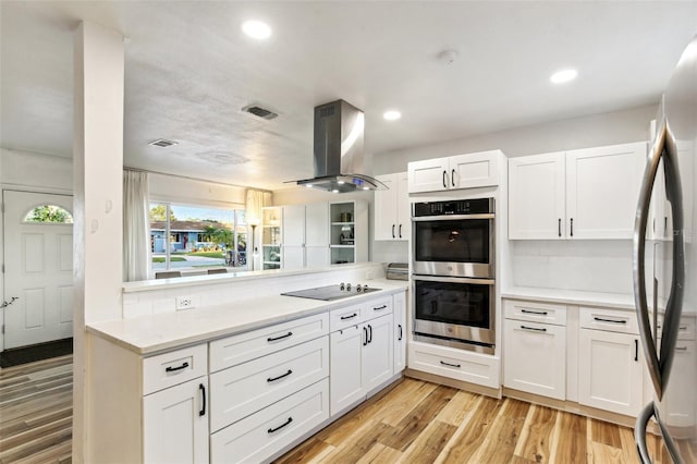 kitchen with white cabinetry, stainless steel appliances, light hardwood / wood-style flooring, backsplash, and island range hood