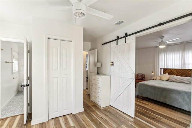 bedroom with hardwood / wood-style floors, a barn door, a closet, and ceiling fan