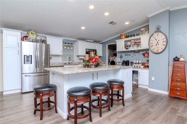 kitchen featuring white cabinetry, stainless steel refrigerator with ice dispenser, backsplash, a center island with sink, and ornamental molding