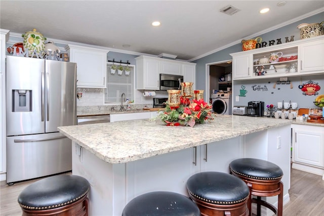 kitchen with stainless steel appliances, a kitchen island, washer / clothes dryer, light hardwood / wood-style floors, and white cabinets