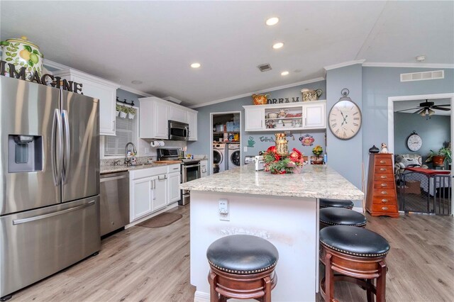 kitchen featuring white cabinets, a kitchen island, light stone counters, stainless steel appliances, and washing machine and clothes dryer