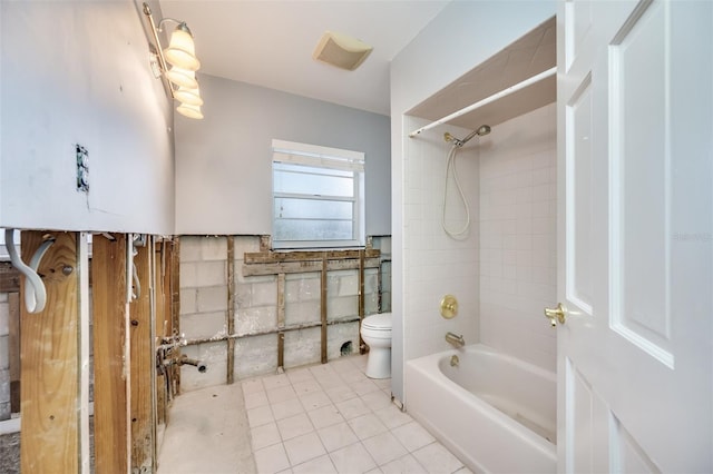 bathroom with tile patterned floors, tiled shower / bath combo, toilet, and tile walls