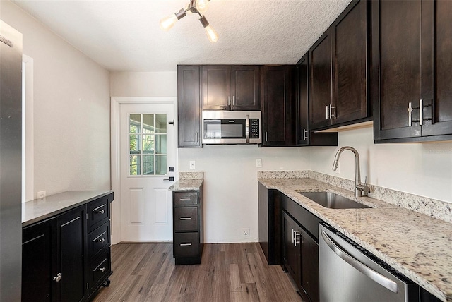 kitchen featuring appliances with stainless steel finishes, light stone counters, dark brown cabinets, sink, and wood-type flooring