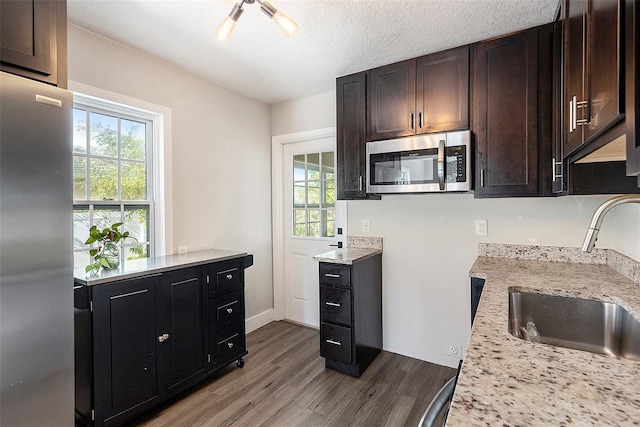 kitchen with dark brown cabinetry, sink, stainless steel appliances, light hardwood / wood-style flooring, and a textured ceiling