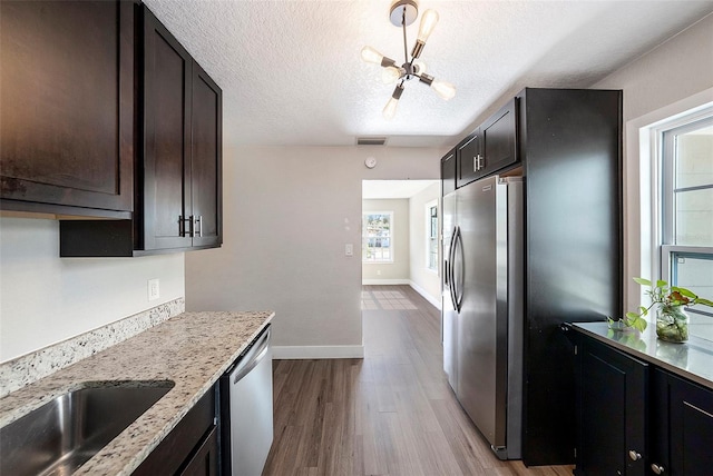 kitchen featuring light stone countertops, appliances with stainless steel finishes, dark brown cabinets, a textured ceiling, and light hardwood / wood-style flooring