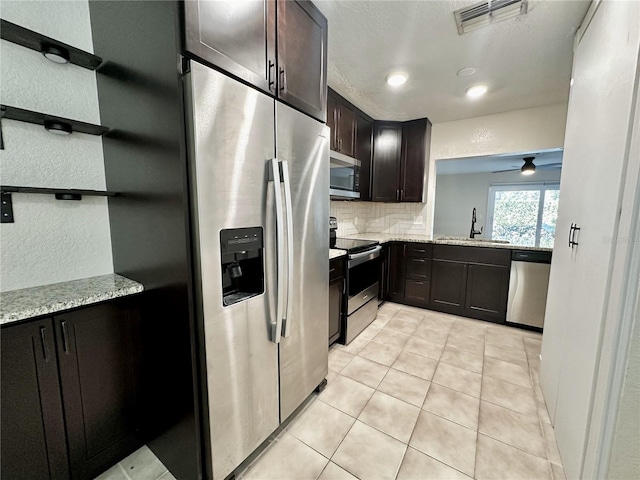 kitchen featuring sink, dark brown cabinets, stainless steel appliances, light stone countertops, and decorative backsplash