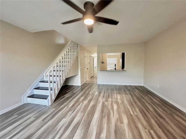 unfurnished living room with a ceiling fan, stairway, wood finished floors, and baseboards