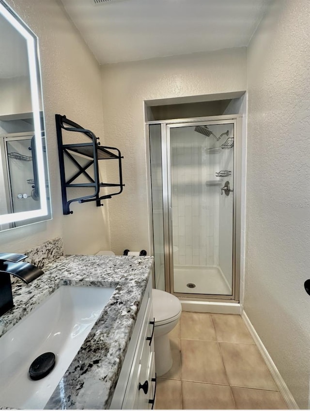 bathroom with a stall shower, tile patterned flooring, baseboards, vanity, and a textured wall