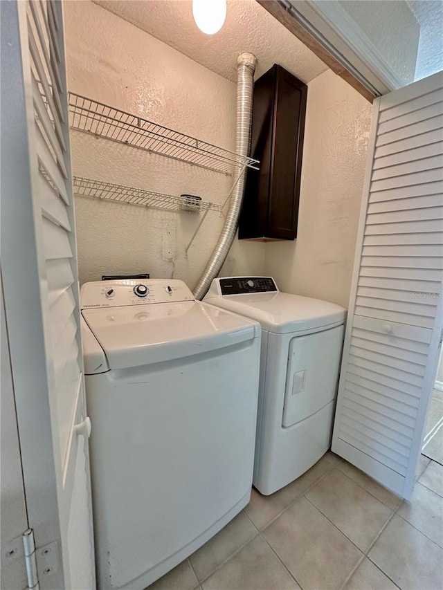 clothes washing area featuring a textured wall, light tile patterned flooring, cabinet space, a textured ceiling, and separate washer and dryer