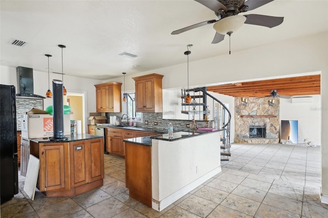 kitchen featuring backsplash, wall chimney range hood, a fireplace, decorative light fixtures, and kitchen peninsula