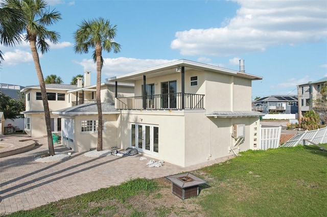 rear view of property featuring french doors, a balcony, an outdoor fire pit, and a lawn