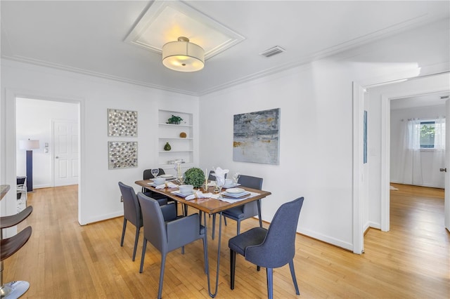 dining space featuring light wood-type flooring, built in features, and crown molding