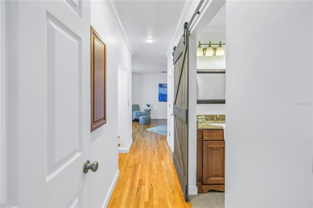 hallway with a barn door, ornamental molding, and light wood-type flooring