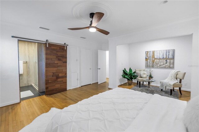 bedroom with ornamental molding, ceiling fan, a barn door, hardwood / wood-style flooring, and connected bathroom