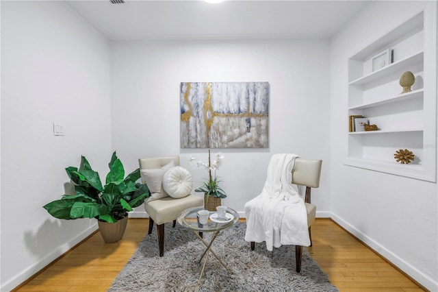 sitting room featuring built in shelves and wood-type flooring