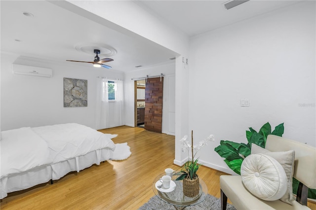 bedroom with a wall unit AC, a barn door, ceiling fan, and wood-type flooring