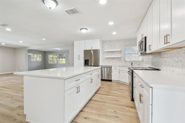 kitchen featuring a center island, backsplash, appliances with stainless steel finishes, white cabinets, and light wood-type flooring