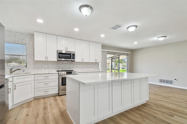 kitchen featuring a center island, stainless steel appliances, white cabinetry, and light hardwood / wood-style floors