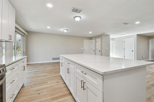 kitchen featuring stainless steel electric range, a kitchen island, light hardwood / wood-style floors, light stone counters, and white cabinetry