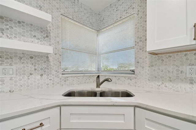 kitchen with light stone counters, white cabinetry, tasteful backsplash, and sink