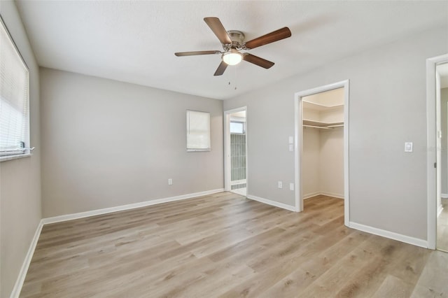 unfurnished bedroom featuring a walk in closet, light hardwood / wood-style floors, multiple windows, and ceiling fan