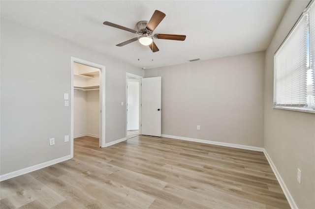 unfurnished bedroom with ceiling fan, light wood-type flooring, a walk in closet, and a closet