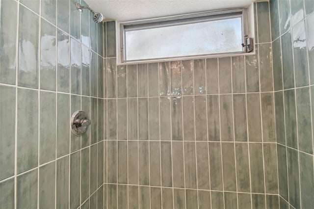 bathroom with a textured ceiling and tiled shower