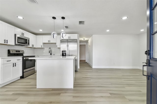 kitchen featuring appliances with stainless steel finishes, light wood-type flooring, white cabinets, a center island, and hanging light fixtures