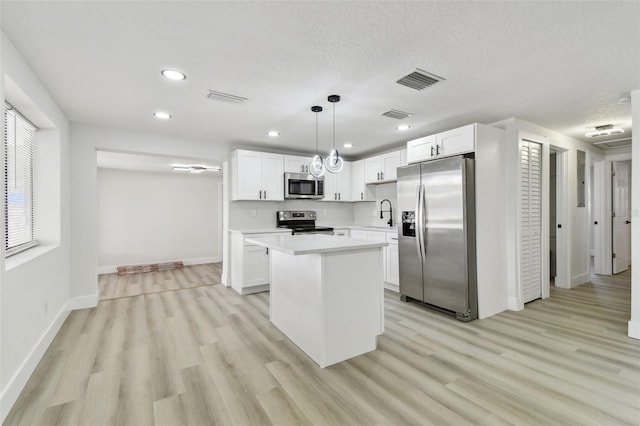 kitchen featuring pendant lighting, a kitchen island, white cabinets, and appliances with stainless steel finishes