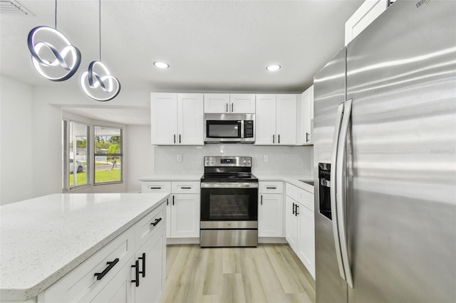 kitchen with light stone countertops, white cabinetry, pendant lighting, appliances with stainless steel finishes, and light wood-type flooring