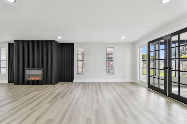 unfurnished living room with a large fireplace, french doors, and light hardwood / wood-style flooring