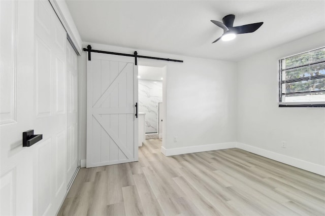 unfurnished room featuring a barn door, light hardwood / wood-style flooring, and ceiling fan