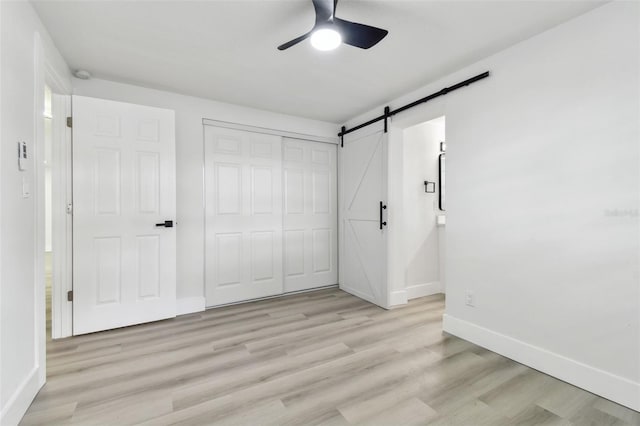 unfurnished bedroom featuring a closet, a barn door, ceiling fan, and light hardwood / wood-style flooring