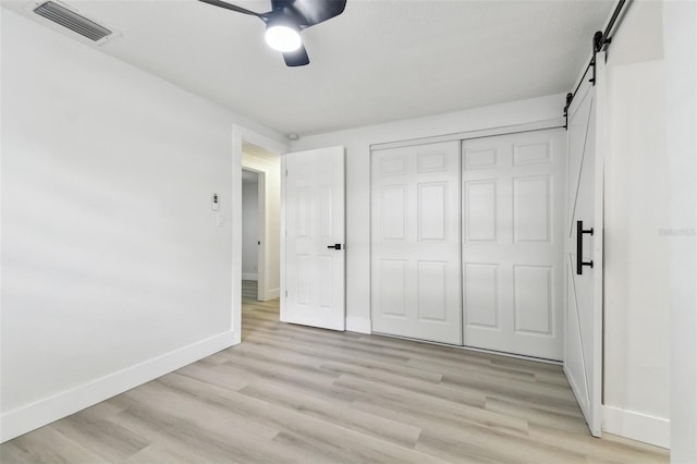 unfurnished bedroom with a barn door, a closet, light hardwood / wood-style flooring, and ceiling fan