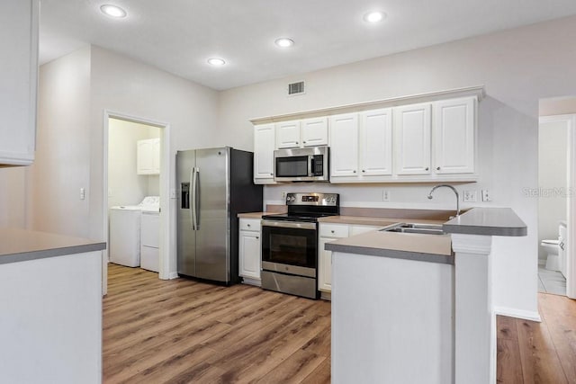 kitchen with kitchen peninsula, stainless steel appliances, sink, separate washer and dryer, and white cabinetry