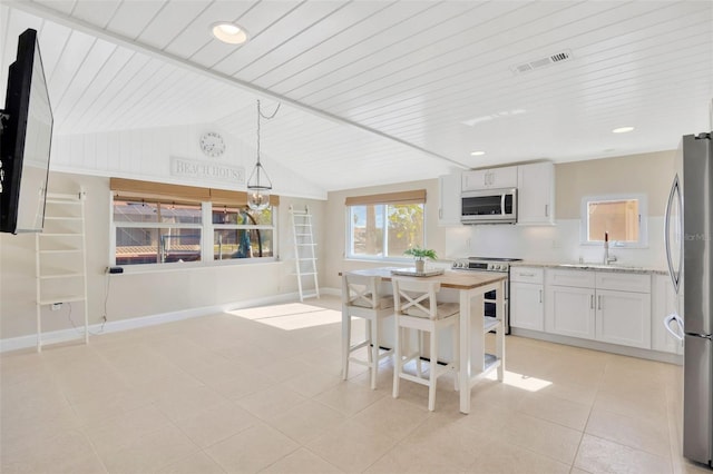 kitchen with white cabinetry, decorative light fixtures, vaulted ceiling, light tile patterned floors, and appliances with stainless steel finishes