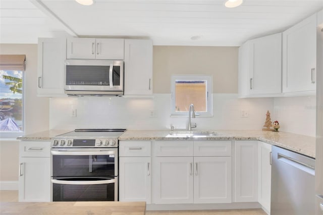 kitchen with tasteful backsplash, sink, white cabinets, and appliances with stainless steel finishes