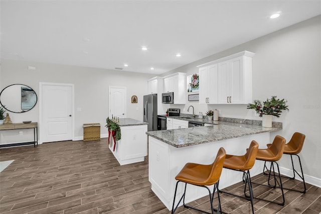 kitchen with kitchen peninsula, white cabinetry, stainless steel appliances, and dark hardwood / wood-style floors