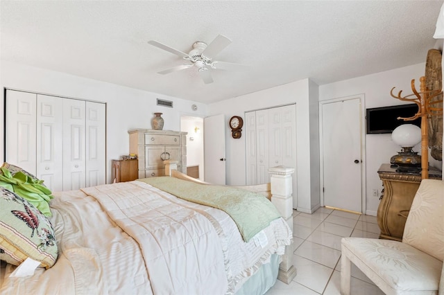 tiled bedroom with a textured ceiling, ceiling fan, and multiple closets