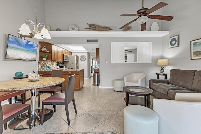 tiled dining room featuring sink, ceiling fan with notable chandelier, and a high ceiling