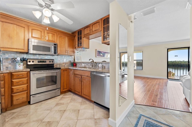kitchen featuring sink, light hardwood / wood-style flooring, decorative backsplash, appliances with stainless steel finishes, and light stone counters