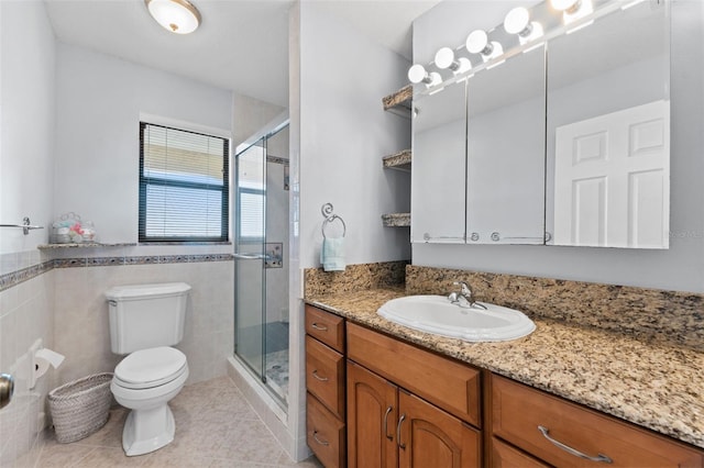 bathroom with tile patterned floors, toilet, vanity, a shower with shower door, and tile walls