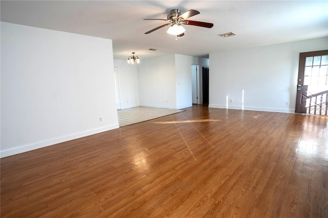 spare room with dark wood-type flooring and ceiling fan with notable chandelier