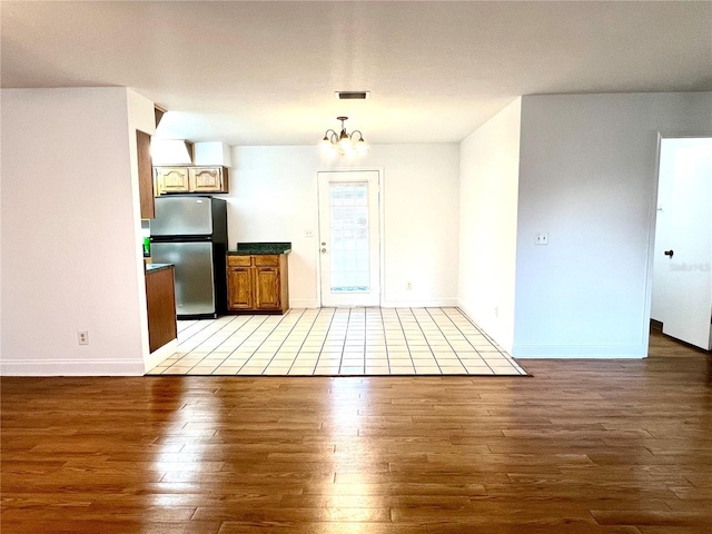 interior space featuring stainless steel fridge, hardwood / wood-style flooring, an inviting chandelier, and pendant lighting